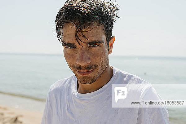 Close-up of handsome young man against sea at beach during sunny day