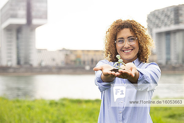 Geschäftsfrau mit Brille  die eine kleine Pflanze hält  während sie am Fluss in der Stadt steht