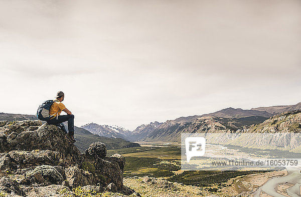Mann mit Rucksack sitzt auf einem Felsen gegen den Himmel  Patagonien  Argentinien