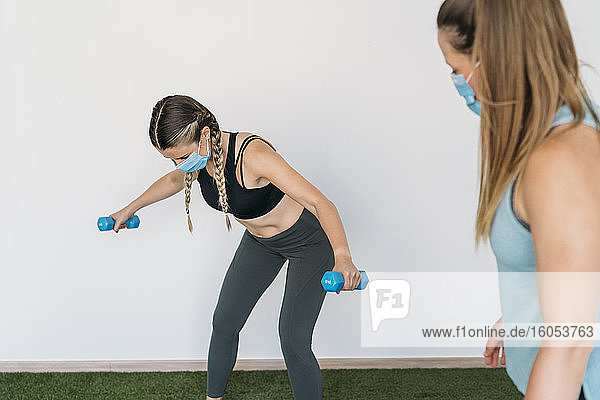 Frau mit Gesichtsmaske beim Training mit Trainer im Fitnessstudio