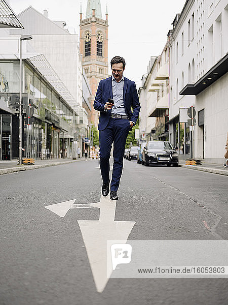 Mature businessman walking on a city street using smartphone