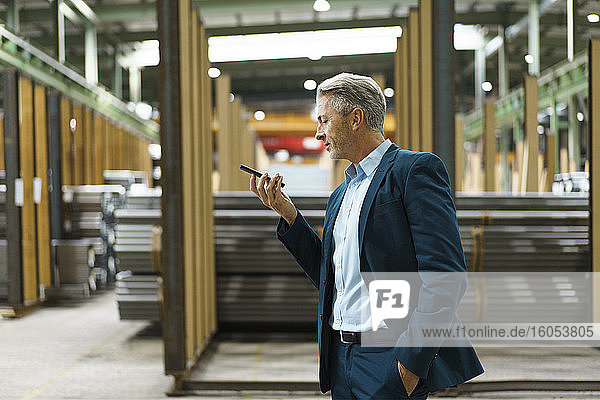 Mature businessman holding mobile phone in a factory