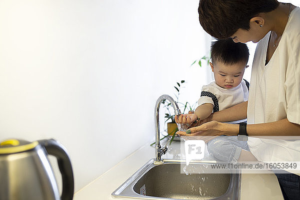 Mutter wäscht niedlichen Sohn die Hände in der Küchenspüle zu Hause