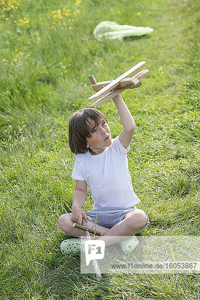 Verspielter Junge fliegt Modellflugzeug  während er auf einer Wiese sitzt