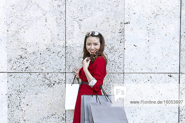 Smiling woman carrying shopping bags while standing by wall
