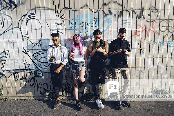 Gruppe von Freunden mit Smartphones an einer Graffiti-Wand in der Stadt