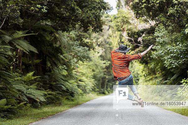 Excited man jumping on country road amidst trees in forest