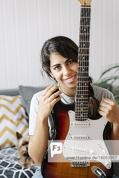 Happy woman holding electric guitar while sitting on sofa at home