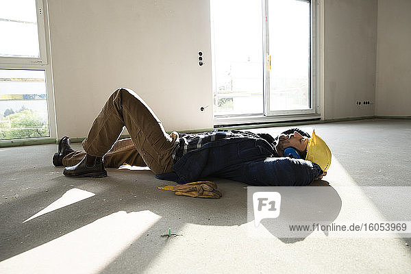 Bauarbeiter mit Händen hinter dem Kopf schlafend auf dem Boden in einem im Bau befindlichen Haus