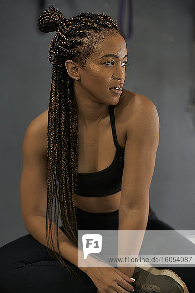 Nahaufnahme einer nachdenklichen Sportlerin mit geflochtenen Haaren  die im Fitnessstudio sitzt