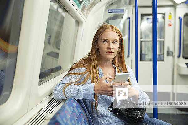 Schöne Frau hält Smartphone im Zug sitzend