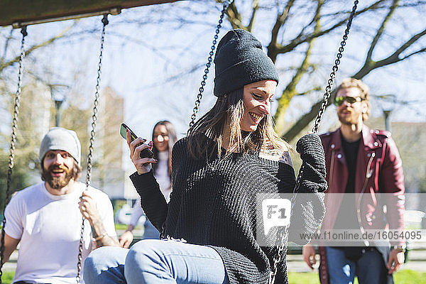 Happy young woman swinging while enjoying with friends in park