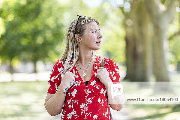 Nachdenkliche Frau steht in einem öffentlichen Park an einem sonnigen Tag