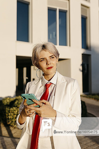 Junge Frau im weißen Anzug benutzt ihr Smartphone in der Stadt