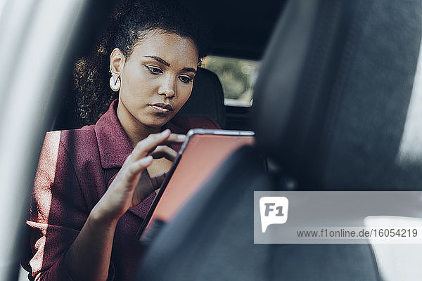 Junge Geschäftsfrau  die im Auto sitzend ein digitales Tablet benutzt