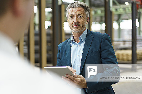 Businessman with tablet looking at colleague in a factory