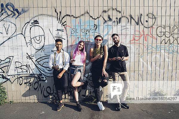 Porträt einer lächelnden Gruppe von Freunden  die an einer Graffiti-Wand in der Stadt stehen