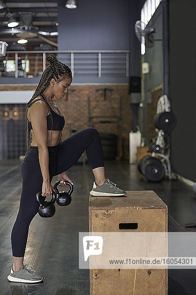 Weibliche Athletin hebt Kettlebells im Stehen im Fitnessstudio