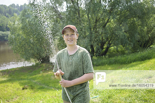 Smiling boy holding hose while standing in forest