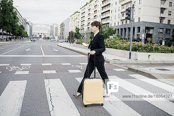 Geschäftsfrau mit Koffer beim Überqueren der Straße in der Stadt