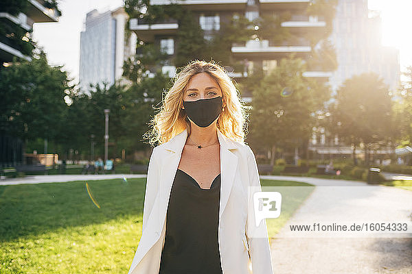 Geschäftsfrau mit Maske auf dem Fußweg in der Stadt an einem sonnigen Tag