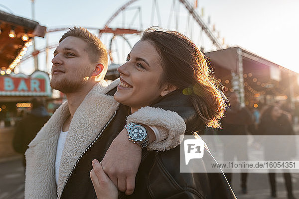 Nahaufnahme eines jungen Mannes mit Hand auf der Schulter seiner Freundin in einem Vergnügungspark bei Sonnenuntergang