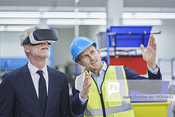 Männlicher Vorgesetzter erklärt dem Manager  der eine VR-Brille trägt  einen Plan in einer Fabrik