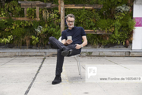 Mature man using smart phone while sitting on chair at yard