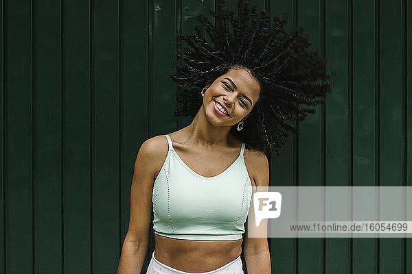 Happy young woman tossing her black curls against green metal door