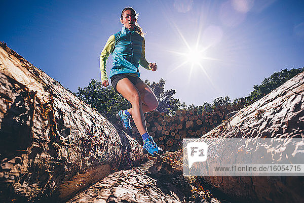 Mature woman running on logs against clear blue sky during sunny day