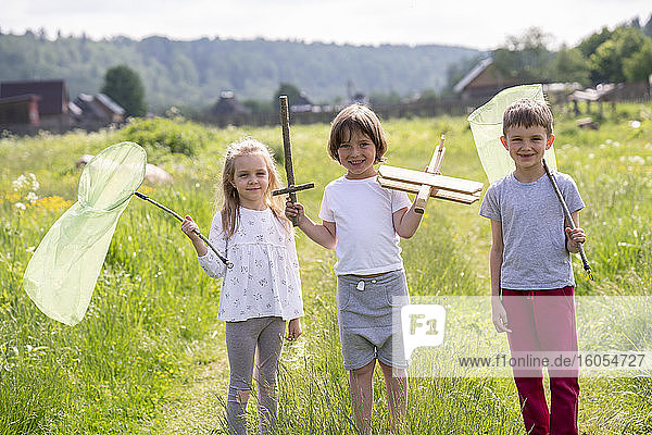 Lächelnde Freunde  die Schmetterlingsnetze und Spielzeug halten  während sie auf einer Wiese stehen