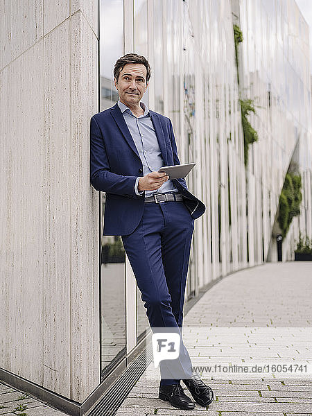 Mature businessman with tablet leaning against a building in the city