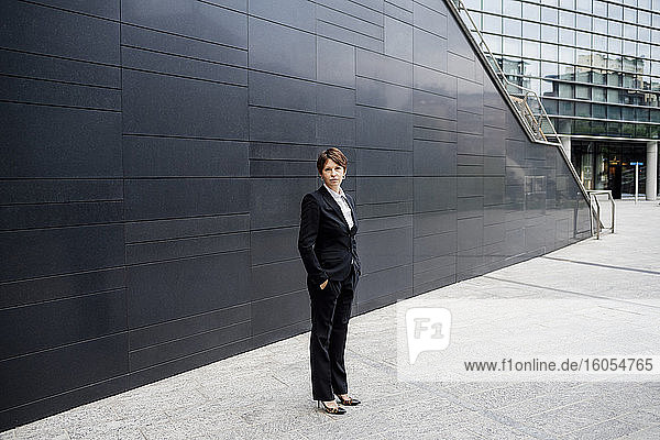 Selbstbewusste Geschäftsfrau steht auf dem Bürgersteig vor modernen Gebäuden in der Stadt