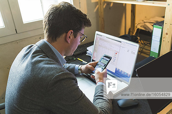 Geschäftsmann mit Smartphone und Laptop am Schreibtisch im Büro