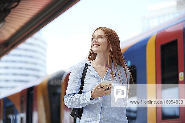 Junge Frau hält Smartphone am Bahnhof
