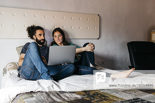 Couple watching movie sitting on bed at home