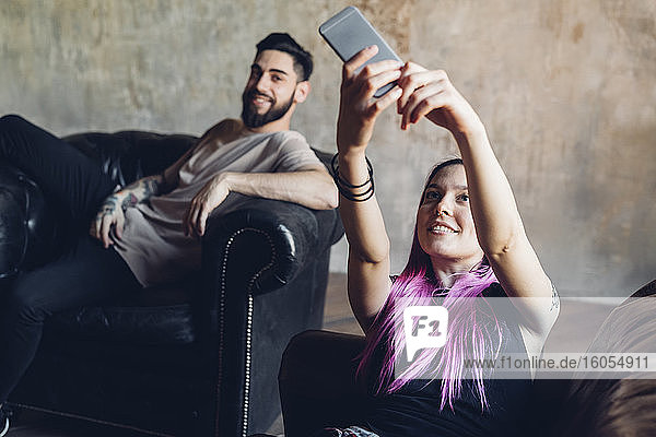 Glückliche junge Frau macht Selfie mit Mann auf Sofa in einem Loft