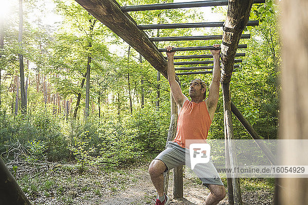 Älterer Mann  der sich beim Training im Park an einem Affengitter aufhängt