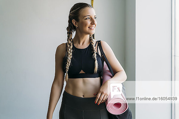 Sportliche Frau trägt Tasche mit Gymnastikmatte im Fitnessstudio