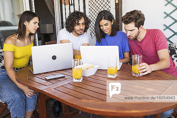 Junge Männer und Frauen teilen sich einen Laptop  während sie am Tisch im Hinterhof sitzen