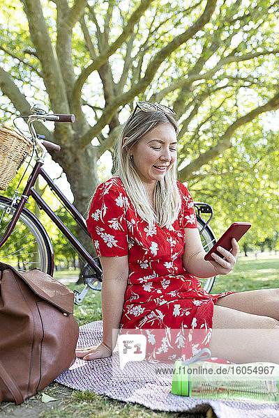 Glückliche Frau  die ein Smartphone benutzt  während sie in einem öffentlichen Park sitzt