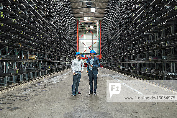 Two businessmen having a meeting in a high rack warehouse of a factory