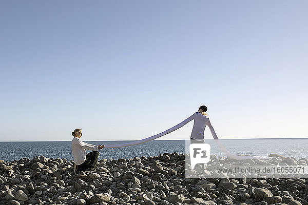 Älterer Mann macht einen Heiratsantrag  während er die lange künstliche Hand der Frau am Strand gegen den klaren Himmel hält