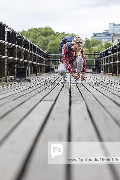 Mid adult woman tying shoelace while crouching on bridge in city