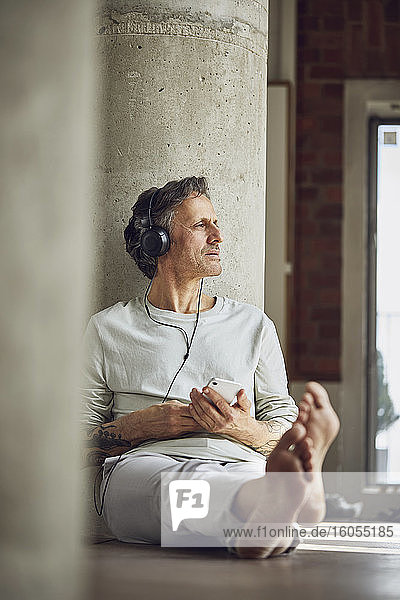 Älterer Mann mit Kopfhörern  der in einer Loftwohnung Musik hört