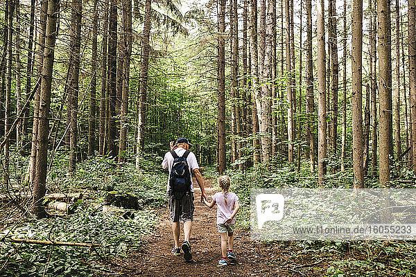 Man holding hands of daughter while hiking in woodland