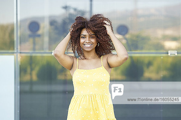 Glückliche junge Frau im gelben Kleid mit Haaren im Haar  die an der Wand steht