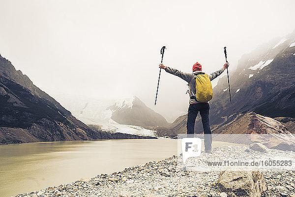 Man with arms outstretched holding hiking poles standing by lake at Patagonia  Argentina