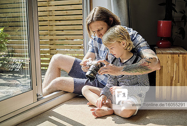 Vater und Sohn beobachten eine Spiegelreflexkamera  während sie zu Hause am Fenster sitzen