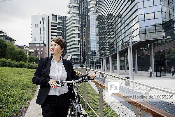 Weibliche Fachkraft mit Fahrrad schaut weg  während sie gegen Gebäude in der Stadt läuft